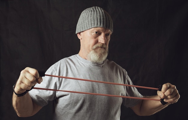 Fitness an elderly stern man stretches a rubber expander