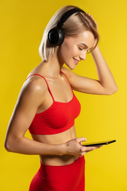 Fitness en muziek zijaanzicht van jonge aantrekkelijke sportieve vrouw in koptelefoon kijken naar haar telefoon