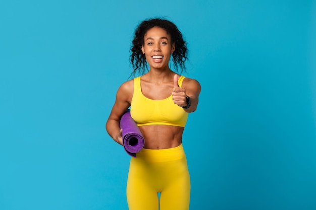 Fitness enthousiaste zwarte dame met yoga mat op blauwe achtergrond