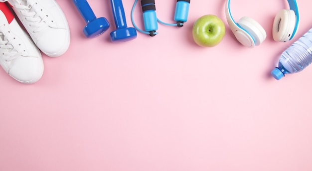 Fitness equipment. Apple, sneakers, water bottle on pink surface.