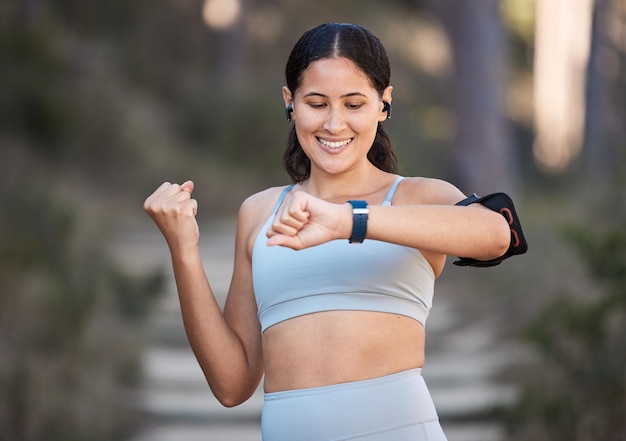 Fitness exercise and woman celebrate goal with watch to check pulse performance and time while in forest or nature for cardio workout and running Female outdoor for training with smartwatch