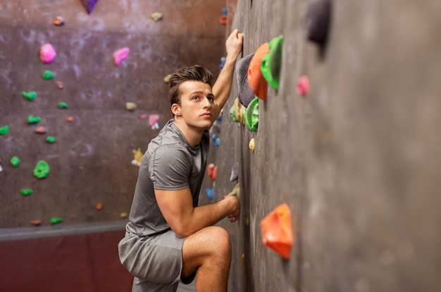 Photo fitness, extreme sport, bouldering, people and healthy lifestyle concept - young man exercising at indoor climbing gym