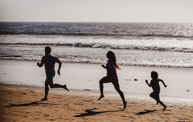 Foto fitness familie rennen op een zandstrand sportieve familie vader moeder en zoontje samen rennen ch