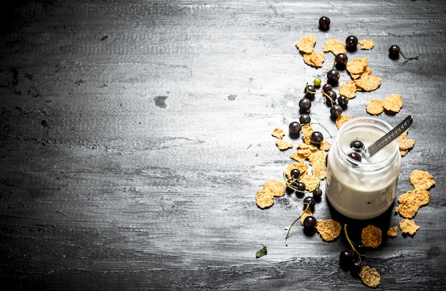 Fitness food. Milk dessert with wheat flakes and wild black currants. On a black wooden table.