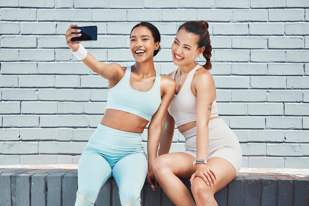 Fitness friends happy and phone selfie for social media picture influencer content and workout after exercise by brick wall Fit athlete females smile for wellness fun and motivation for internet