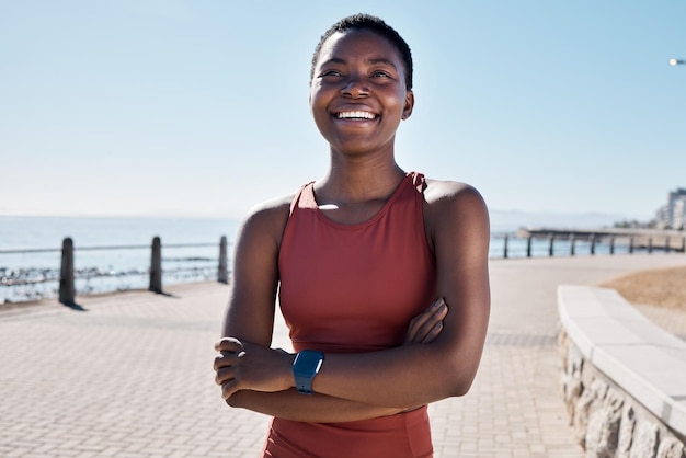 Fitness gelukkige zwarte vrouw en denken op strandstoet van visie, mentaliteit en motivatie voor zomerlichaamsdoelen, gezonde lichaamsbeweging en wellness Vrouwelijke sportatleet glimlach en armen gekruist op zee