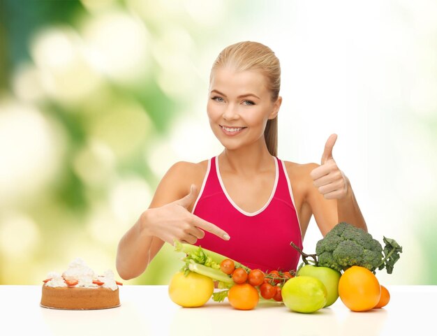 fitness, gezondheidszorg en dieet concept - lachende vrouw met fruit en cake wijzend op gezonde voeding