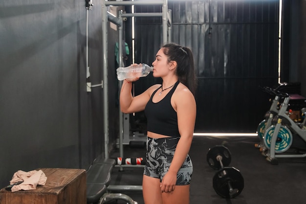 Fitness girl drinking water in the gym resting between sets