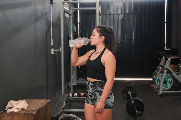 Foto ragazza di fitness che beve acqua in palestra che si riposa tra i set