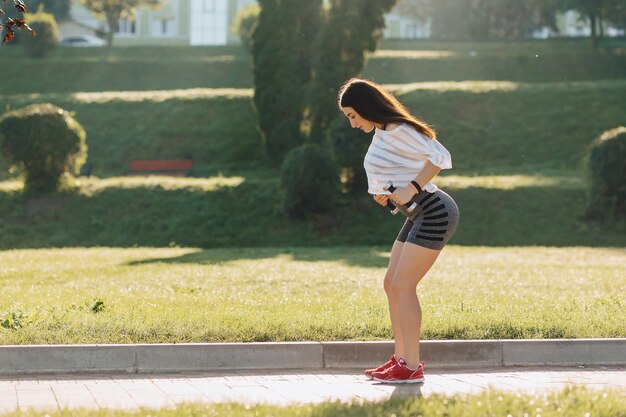 フィットネス女の子の外の芝生で夕日にダンベルでのエクササイズ