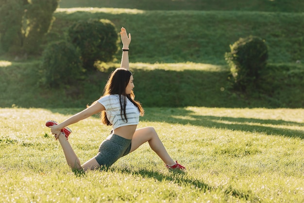 Fitness girl making stretching exercises outside on sunshine an grass