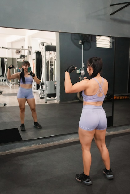 Fitness girl showing muscle taking photos in the gym mirror