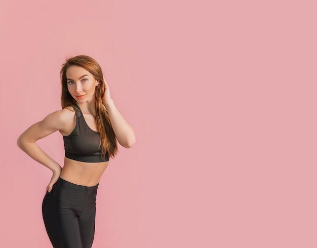 Fitness girl smiling in black sportswear on a pink space