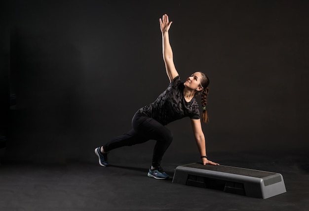 Фитнес-девушка на ступеньке на платформе с одной рукой делает упражнения Занимается спортом на черном