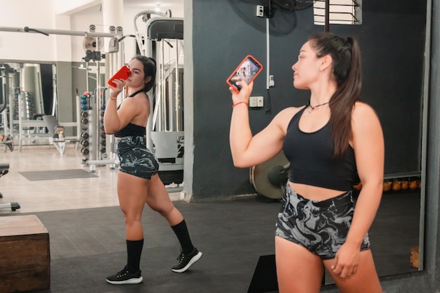 Fitness girl taking photos in front of the gym mirror showing training results