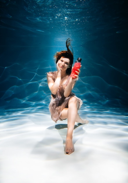 Fitness girl with colorful smoothie. Freshness under water, swims and dives.