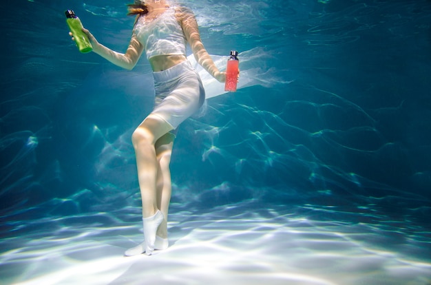 Fitness girl with colorful smoothie. Freshness under water, swims and dives.