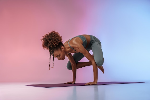 Fitness glimlachende vrouw die yoga beoefent op mat op studio achtergrond met kleurenfilter