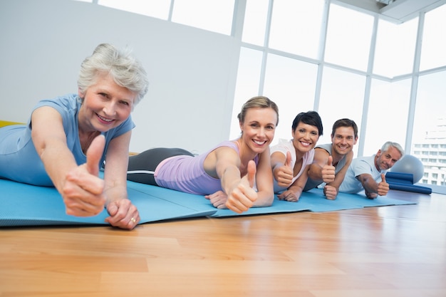 Fitness group gesturing thumbs up at yoga class