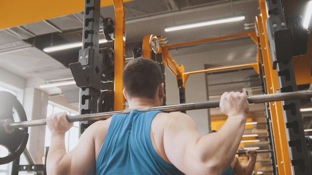 Фитнес тренажерный зал мускулистый мужчина выполняет приседания со штангой вид сзади