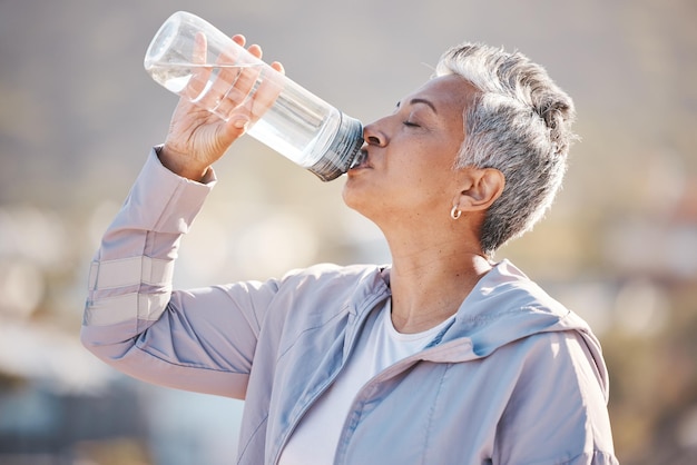 Fitness health and senior woman drinking water for hydration on outdoor cardio run exercise or retirement workout Marathon training bottle and profile of runner running in Rio de Janeiro Brazil