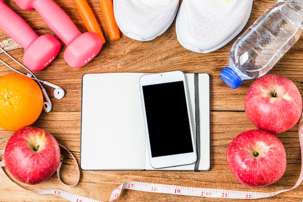 Fitness, healthy and active lifestyles Concept, Bottle of water, dumbbells, sport shoes, smartphone with headphone and apples on wood background. copy space for text. Top view