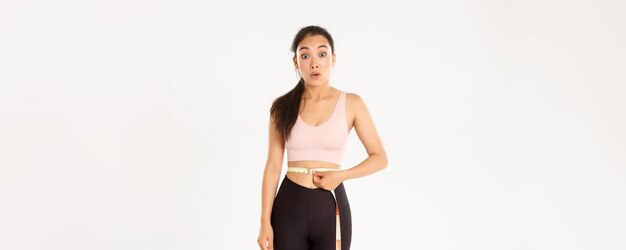 Fitness healthy lifestyle and wellbeing concept surprised asian girl on diet sportswoman wrap measur