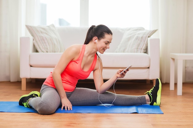 fitness, home, technology and diet concept - smiling teenage girl streching on floor with smartphone and earphones at home