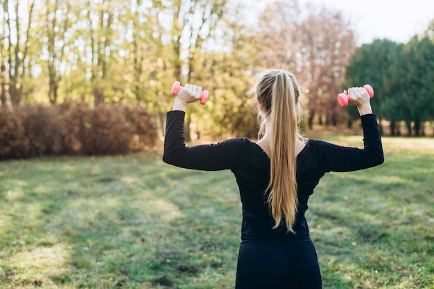 Fitness in het park, meisje met halters, achteraanzicht.