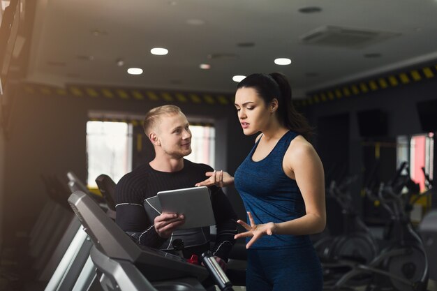 Fitness instructeur helpt jonge vrouw op elliptische trainer. Coach bespreken trainingsplan met meisje op loopband. Cardiotraining in de sportschool, gezonde levensstijl, kopieer ruimte