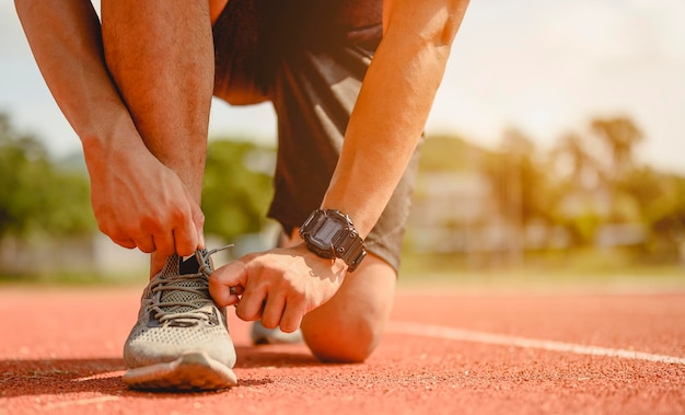 Fitness, joggen, hardlopen, lichaamsbeweging, levensstijl en gezond concept. De jonge man gebruikt hun handen om hun schoenen te strikken om te joggen op de atletiekbaan rond het voetbalveld.