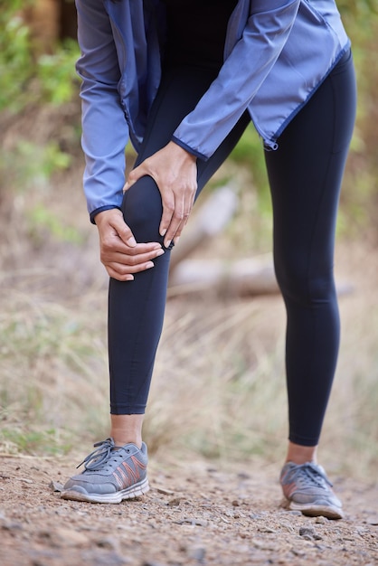 Foto dolore al ginocchio fitness e massaggio alle mani della donna in allenamento escursionistico nella foresta o incidente di corsa e zoom del corpo per l'assicurazione sanitaria lesioni alle gambe dolori articolari o artrite del corridore atleta a rischio medico