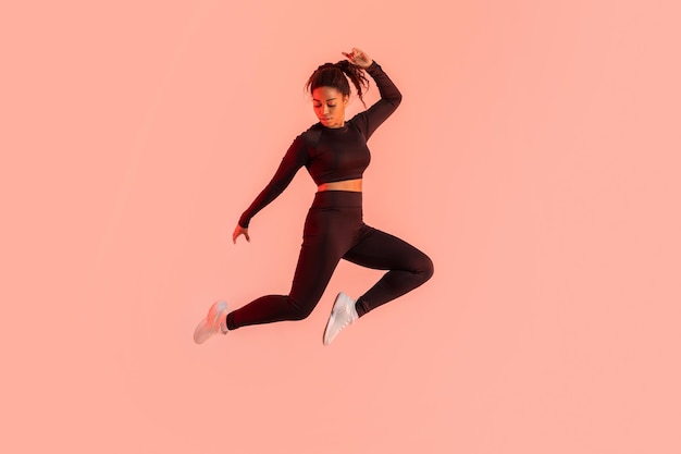 Fitness levensstijl gemotiveerde zwarte dame die in de lucht springt over perzik neon achtergrond die een sprong maakt