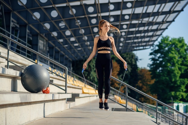 Concetto di stile di vita e di forma fisica - donna che fa gli sport all'aperto. ragazza con la corda per saltare.