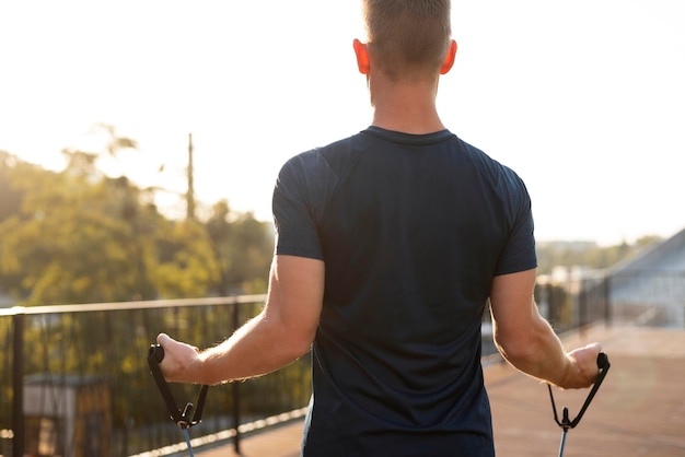 Фитнес-мужчина делает упражнения с растяжкой, стоя спиной на закате, работает с резинкой