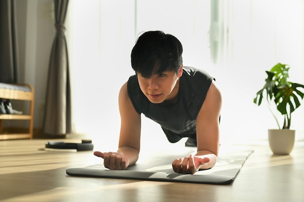 Fitness man doing plank exercise on mat during morning training at home.