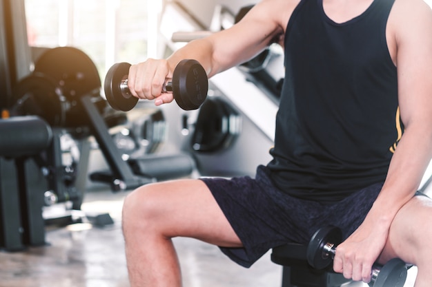 Fitness man doing weights exercises with dumbbell sitting at the gym