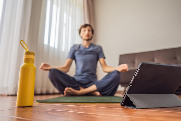 Fitness man exercising on the floor at home and watching fitness videos in a tablet People do sports online because of the coronovirus Focus on the tablet