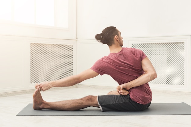 Fitness man at legs stretching training. Young sporty guy makes aerobics exercise at gym. Healthy lifestyle, gymnastics concept