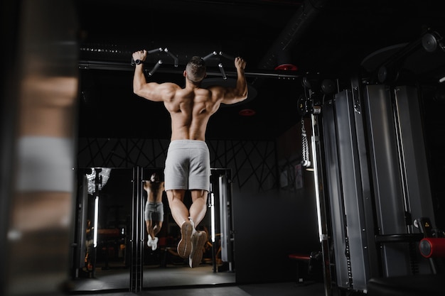 Fitness man oppompen van spieren doen pull-ups oefeningen in sportschool naakte torso. Knappe sterke atletische mannen oppompen van rugspieren training fitness en bodybuilding concept achtergrond