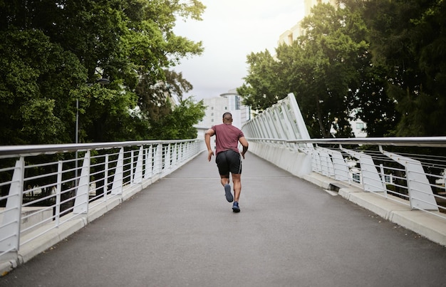 Fitness man and running in the city park for healthy exercise cardio workout or training in the outdoors Active athletic male runner in sports activity run or exercising outside on city bridge