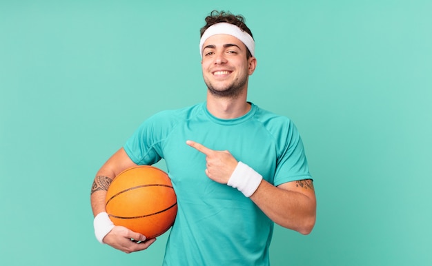 Fitness man smiling cheerfully, feeling happy and pointing to\
the side and upwards, showing object in copy space