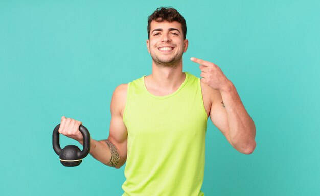 Fitness man smiling confidently pointing to own broad smile, positive, relaxed, satisfied attitude