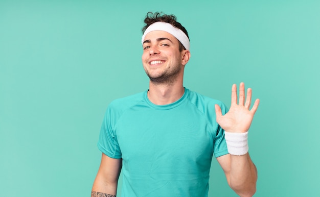 Fitness man smiling happily and cheerfully, waving hand, welcoming and greeting you, or saying goodbye