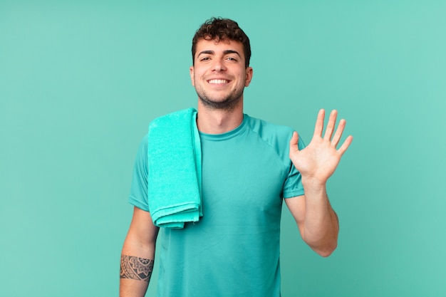 Fitness man smiling happily and cheerfully, waving hand, welcoming and greeting you, or saying goodbye