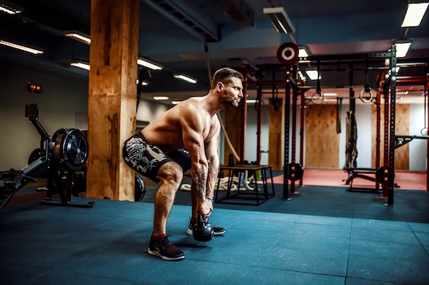 Fitness man swingende kettlebells in de sportschool