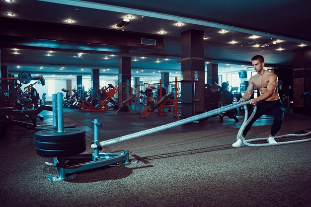 Fitness man working out with battle ropes at gym.