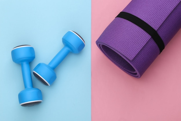 Fitness mat and dumbbells on pink blue pastel  background. Healthy lifestyle, fitness training. Top view