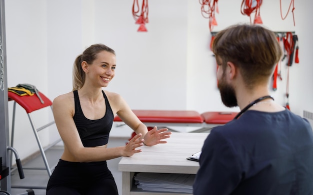 Fitness meisje en fysiotherapeut arts met plezier praten in revalidatiekliniek kantoor