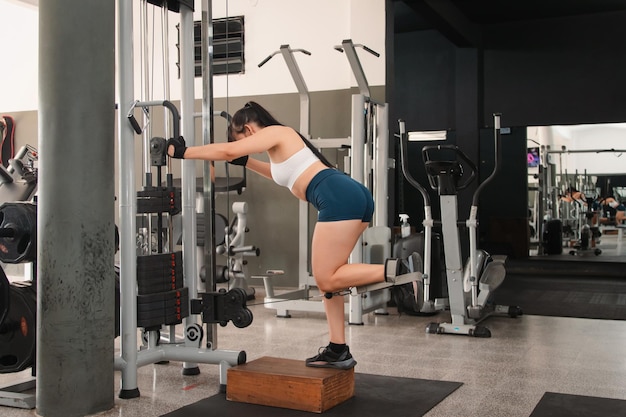 Fitness meisje met behulp van de katrol om een beenoefening uit te voeren in de sportschool